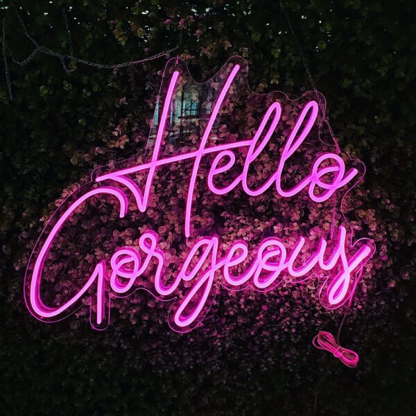 A glowing neon sign with the phrase 'Hello Gorgeous' in vibrant colors, evoking elegance and positivity.