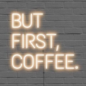 A glowing neon sign with the phrase 'BUT FIRST, COFFEE' in bold letters, evoking energy and motivation for the day.