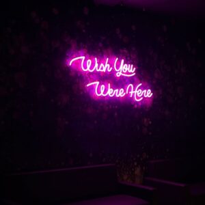 A glowing neon sign with the phrase 'Wish You Were Here' in vibrant colors, evoking sentimentality and longing for loved ones.