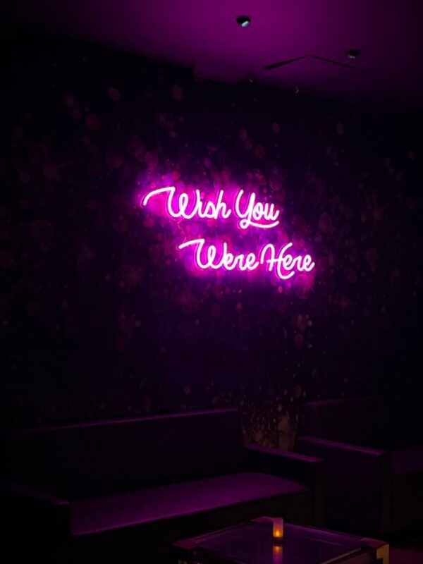 A glowing neon sign with the phrase 'Wish You Were Here' in vibrant colors, evoking sentimentality and longing for loved ones.