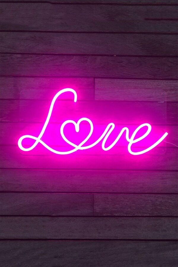 Neon sign spelling out the word 'LOVE' in cursive, glowing in a warm pink light against a dark background.